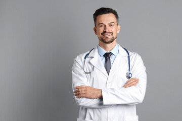 Smiling doctor with stethoscope on grey background, space for text