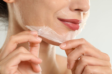 Woman peeling off face mask on light grey background, closeup