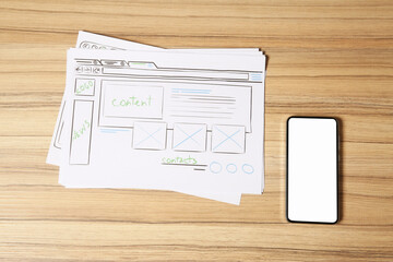 Website development. Sketches of wireframes and smartphone on wooden table, flat lay