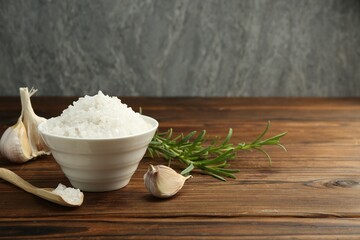 Sea salt in bowl, garlic and rosemary on wooden table. Space for text