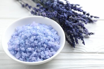 Natural sea salt in bowl and lavender on white wooden table, closeup