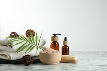 Spa treatment. Towels, sea salt, brush, bottles of cosmetic products and palm leaf on white marble table, space for text