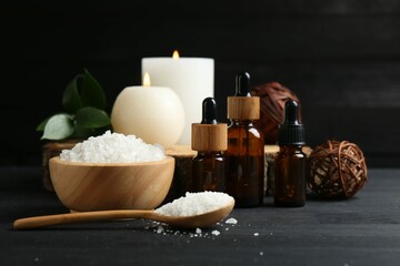 Composition with cosmetic products and candles for spa treatment on black wooden table, closeup