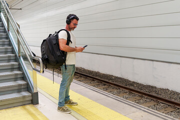Middle-Aged Man in Casual Clothing with Backpack Using Smartphone for E-Ticket While Waiting for Train at Station