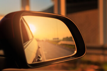 The sun is reflected in the mirror, evening road. View in the side rear view mirror of a red car...