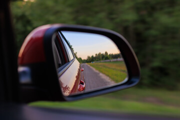 The sun is reflected in the mirror, evening road. View in the side rear view mirror of a red car...