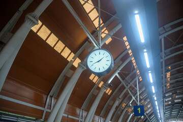 A large, round clock is suspended from the ceiling of a modern train station in Jakarta, Indonesia....