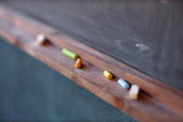 Close up of colorful chalk pieces on blackboard shelf in primary school classroom or kindergarten copy space
