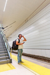 Fototapeta premium Middle-Aged Man in Casual Clothing with Backpack Using Smartphone for E-Ticket While Waiting for Train at Station