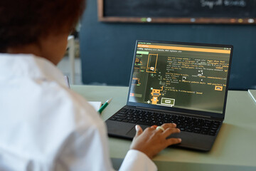 Over shoulder view of unrecognizable young girl using laptop with programming code lines on screen...