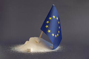 A mountain of granulated sugar and the flag of the European Union in close-up on a light background. Europe is one of the main sugar producers in the world.