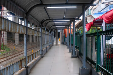 A covered pedestrian walkway near a train station in Jakarta, Indonesia, features metal fencing and a tiled floor. 