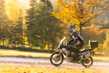 Motorcyclist rides through scenic autumn forest trail.