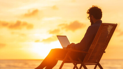 Obraz premium silhouette of a person working on his laptop outdoors on the beach at golden hour, back view