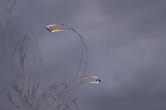 Aerobatic airplanes with smoke trails in cloudy sky.