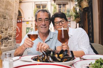 Senior couple toasting, holding glasses of beer and enjoying lunch with mussels in a restaurant