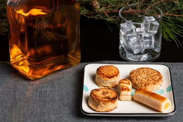 Plate with a wide variety of typical Christmas sweets along with a bottle of liquor and a glass of ice, close-up.