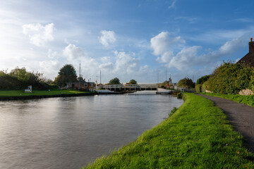 Fototapeta premium A swing bridge on a canal with a green bank and blue sky with clouds
