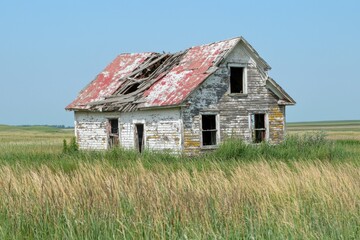 Obraz premium An abandoned rural farmhouse with a collapsed roof, peeling paint, and tall grass surrounding it, with open space in the foreground for text, evoking a sense of solitude and time passing. 