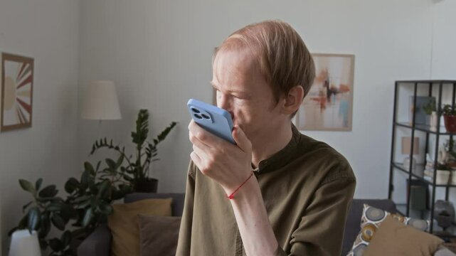 Man with visual impairment recording voice message for friend on smartphone at home