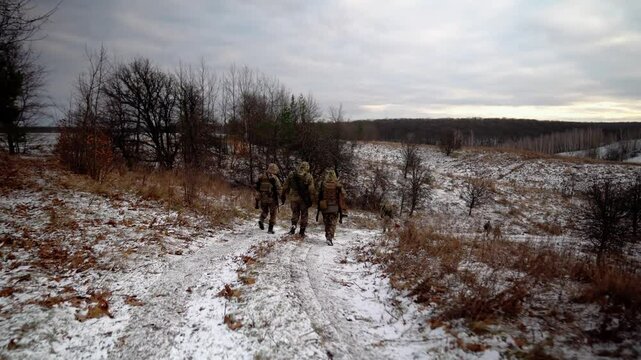 Soldiers in full gear walk across a field in winter. Ukrainian soldiers patrol the area. Soldiers with machine guns go to the shooting range.