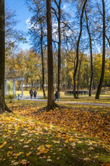 A park with a white gazebo and a few people walking around