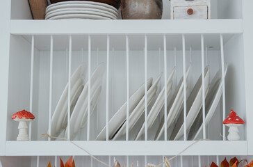 White dish rack displaying neatly arranged plates and charming decorative mushrooms
