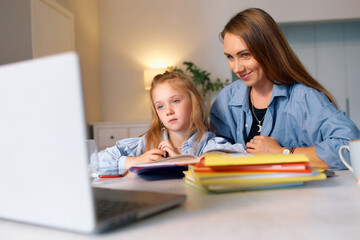 Red-haired schoolgirl with her mother sitting at a desk and doing homework for school