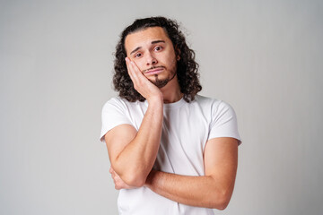 A young man stands thoughtfully against a plain background, expressing contemplation