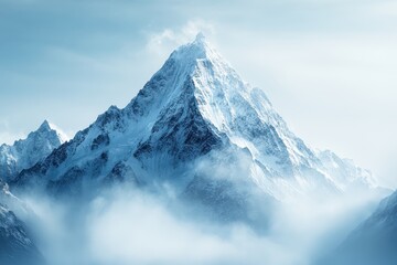 Majestic snow-capped mountain peak shrouded in mist under a clear blue sky at dawn
