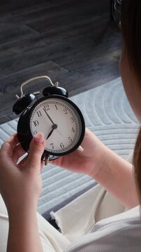 Close up shot of a Caucasian woman hands changing time in clock at home. Concept of a summertime or wintertime turning. Vertical video.