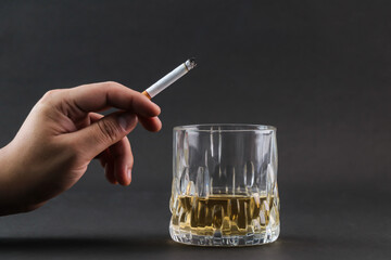 One hand putting cigarette ash into a glass of whiskey.