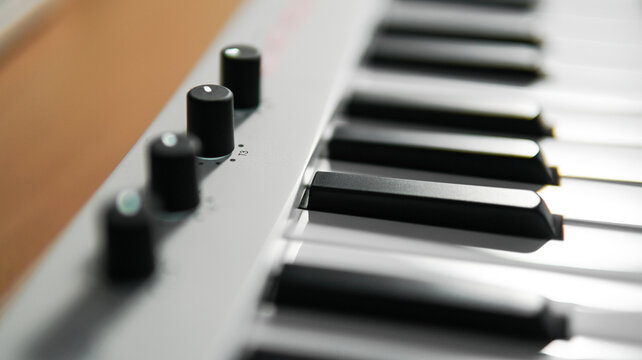 Closeups of a piano, midi controller, or keyboard with adjustable knob on a wooden table. Home studio or music equipment concept.