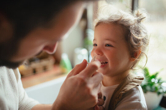 Sick girl with cold at home has stuffy nose. Father helping little daughter to breath better, using nasal spray in his nose.