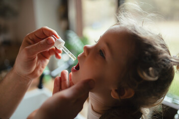 Father giving his daughter medicine with medicine dropper, cough syrup or fever medicine. Sick girl...