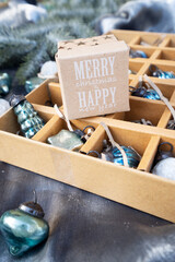 Box of vintage Christmas ornaments in green and blue on silver fabric backdrop, ready for holiday decoration.