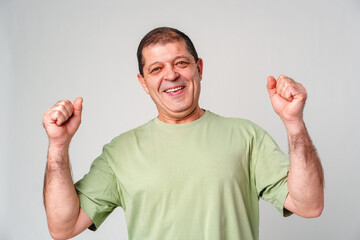 Happy elderly man celebrating a victory with joyful gestures in a light-colored setting