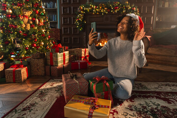 Merry Christmas. African woman in Santa hat having video chat in smartphone. Blogger in festive mood recording video in social network. Girl having video call with friends family celebrating Christmas