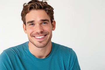 A young man in a blue tshirt smiling in front of a white wall