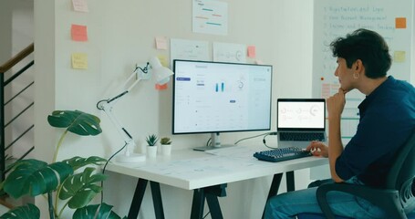 Positive young freelance Asia male casual wear use computer remote working on desk in living room at home office. Work from house, financial plan, remotely digital nomad job and Gen Z talent concept. - Powered by Adobe