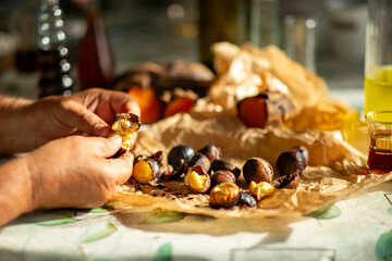 Hands peeling roasted chestnut with more chestnuts on crumpled paper