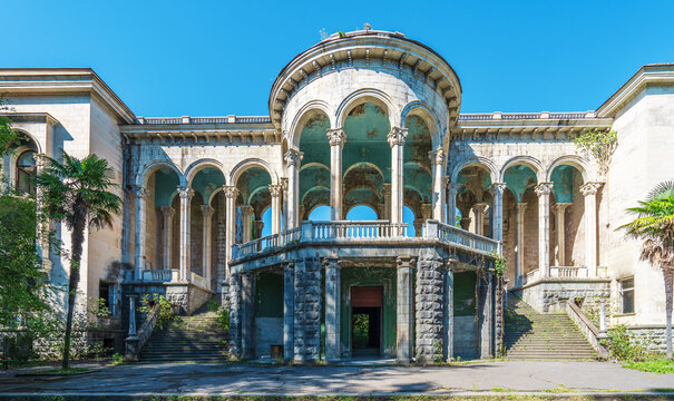 Facade of abandoned Medea sanatorium in Tskaltubo, Georgia. Neoclassical architecture with tall columns and grand arches shows signs of decay, surrounded by nature.