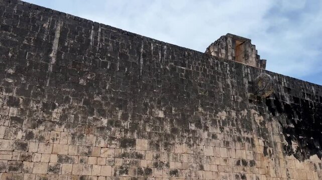 Handheld wide tilting up shot of the stone ring on the court wall at the Great Mayan Ball Court in Chichen Itza, Mexico. 4K