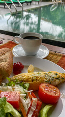 A delicious breakfast of omelette, salad, and coffee by a poolside, perfect for a relaxing vacation or holiday brunch