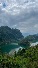 Obraz premium Serene tropical landscape with lush green mountains and a winding river under a cloudy sky, ideal for Earth Day themes