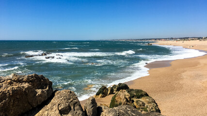 A beautiful sunny beach with waves crashing against rocks, ideal for representing summer vacations and coastal relaxation
