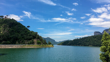 Scenic view of a tranquil lake surrounded by lush green hills under a clear blue sky, ideal for summer vacations