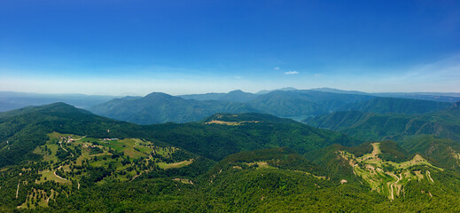 Obraz premium A panoramic view of lush green mountains and valleys under a clear blue sky, ideal for summer travel and adventure