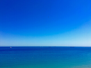 A clear blue sea under a bright sky, symbolizing summer vacation and tranquility, with distant ships on the horizon