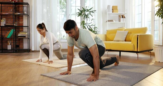 Indian Asian young couple joyfully practicing yoga together in their lavish home, executing Ek Pad Prasarita Padasana, or One-Legged Wide-Legged Forward Bend pose